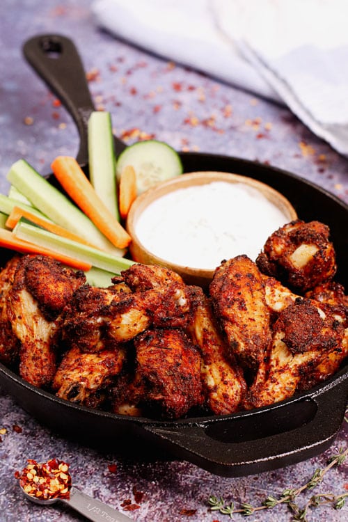 Air fryer chicken wings dry rub recipe bite shot, served on a cast iron skillet with ranch dipping sauce and vegetable sticks.