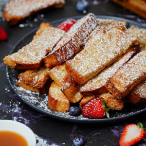 Air fryer French toast sticks with powdered sugar on top, caramel dipping sauce and fresh berries.