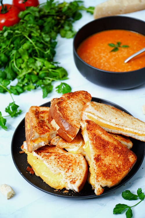 Air fryer grilled cheese sandwich recipe bite shot, stacked on a black plate with tomato soup.