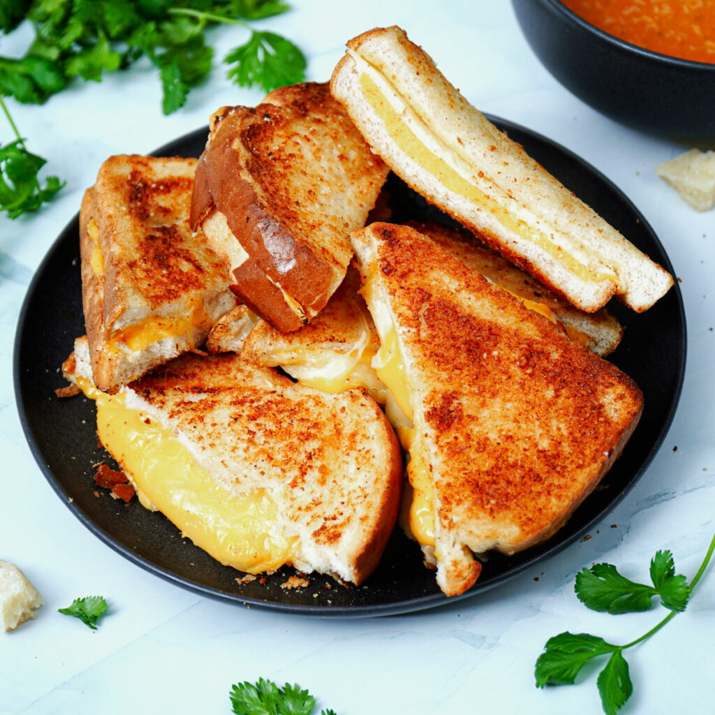 Air fryer grilled cheese sandwich stacked on a black plate with tomato soup on the side.