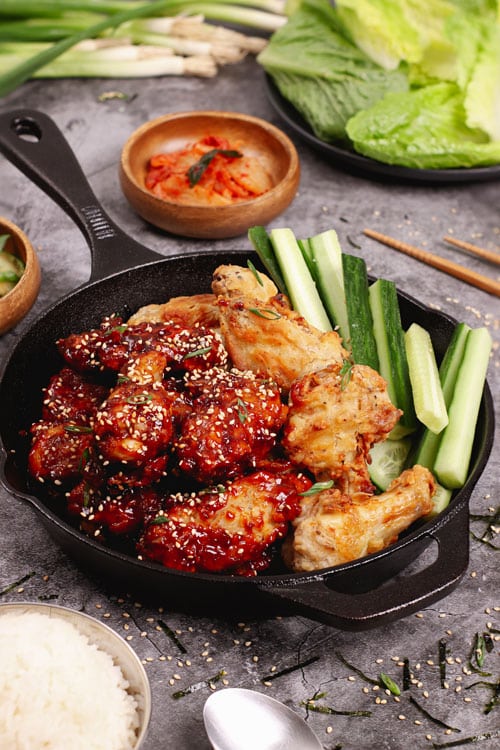 Air fryer Korean fried chicken wings recipe bite shot, served with cucumber sticks, rice, and kimchi.