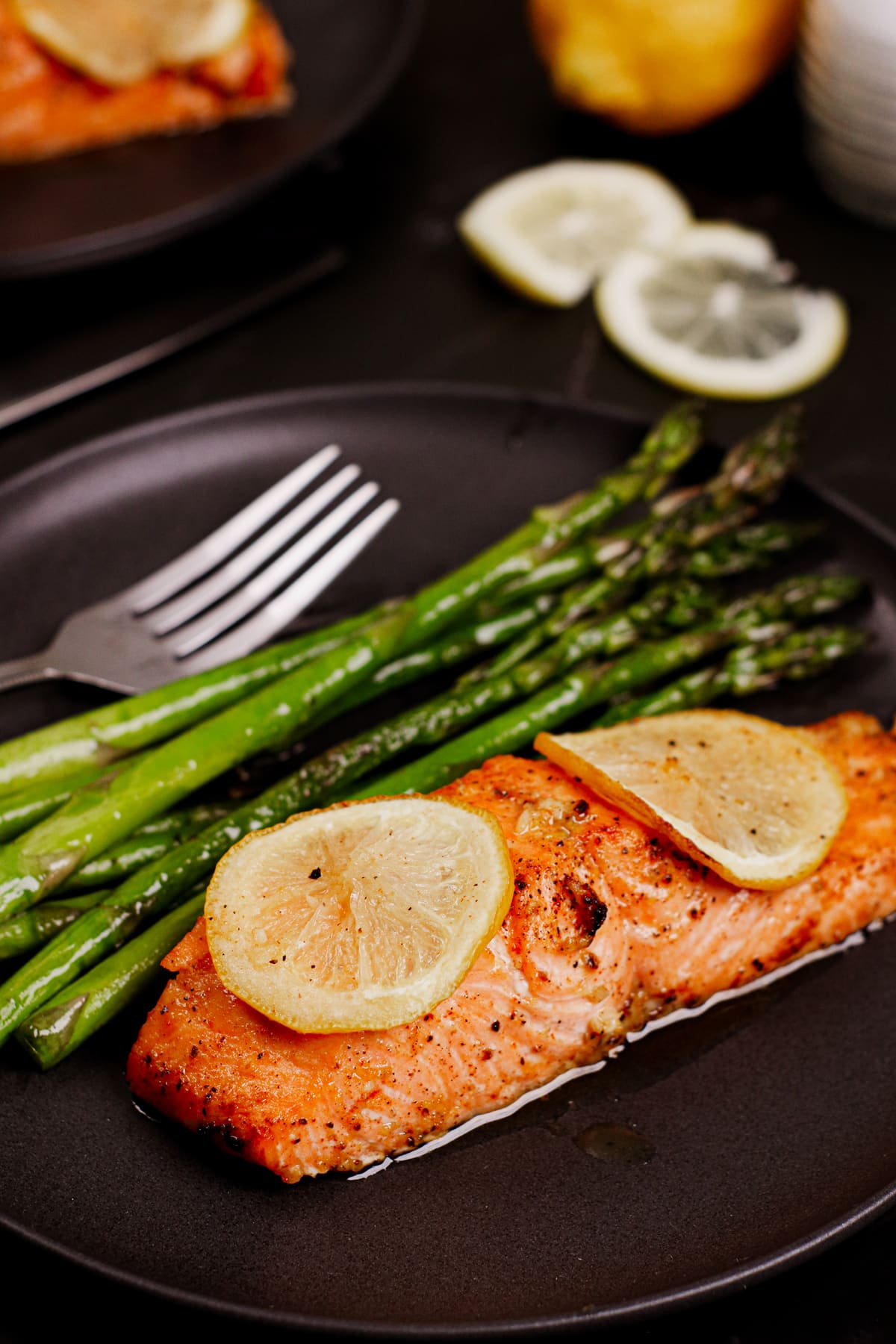 Air fryer lemon butter salmon recipe bite shot, served with lemon slices on top and roasted asparagus