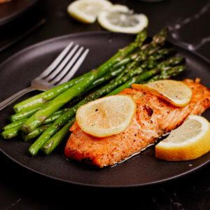 Air fryer lemon butter salmon served with lemon slices on top and roasted asparagus on the side