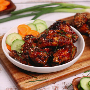 Air fryer Mongolian chicken wings on a wooden serving board with carrots and cucumber slices.
