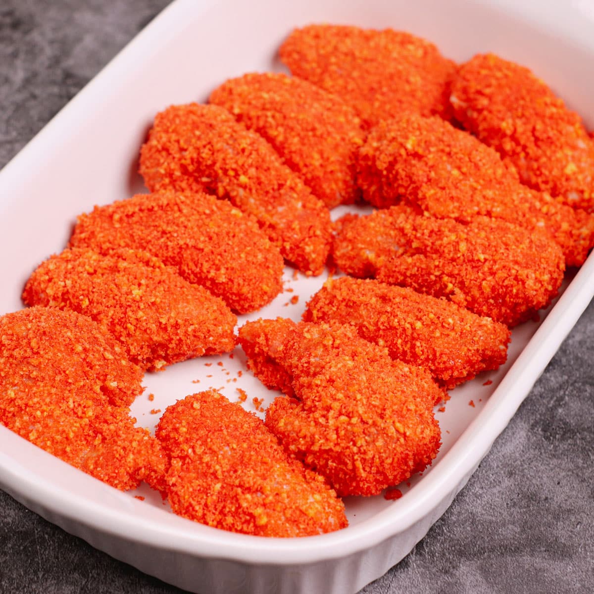 Uncooked, breaded cheeto wings in a baking dish