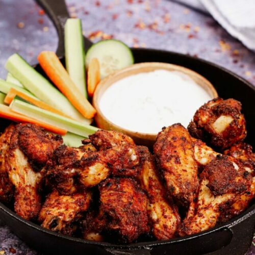 Air fryer chicken wings dry rub recipe bite shot, served on a cast iron skillet with ranch dipping sauce and vegetable sticks.