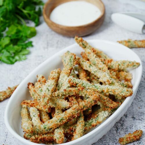 Air fryer green bean fries recipe bite shot, served on a baking dish with ranch dipping sauce.