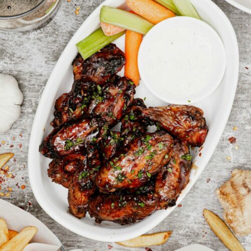 Air fryer honey garlic chicken wings recipe biteshot, on a serving dish with carrots, celery sticks and ranch dipping sauce.