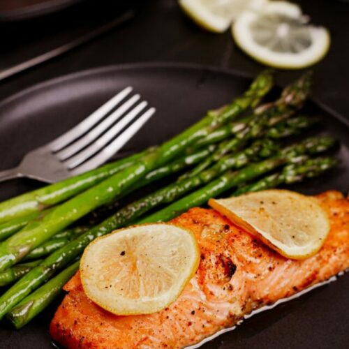 Air fryer lemon butter salmon recipe bite shot, served with lemon slices on top and roasted asparagus