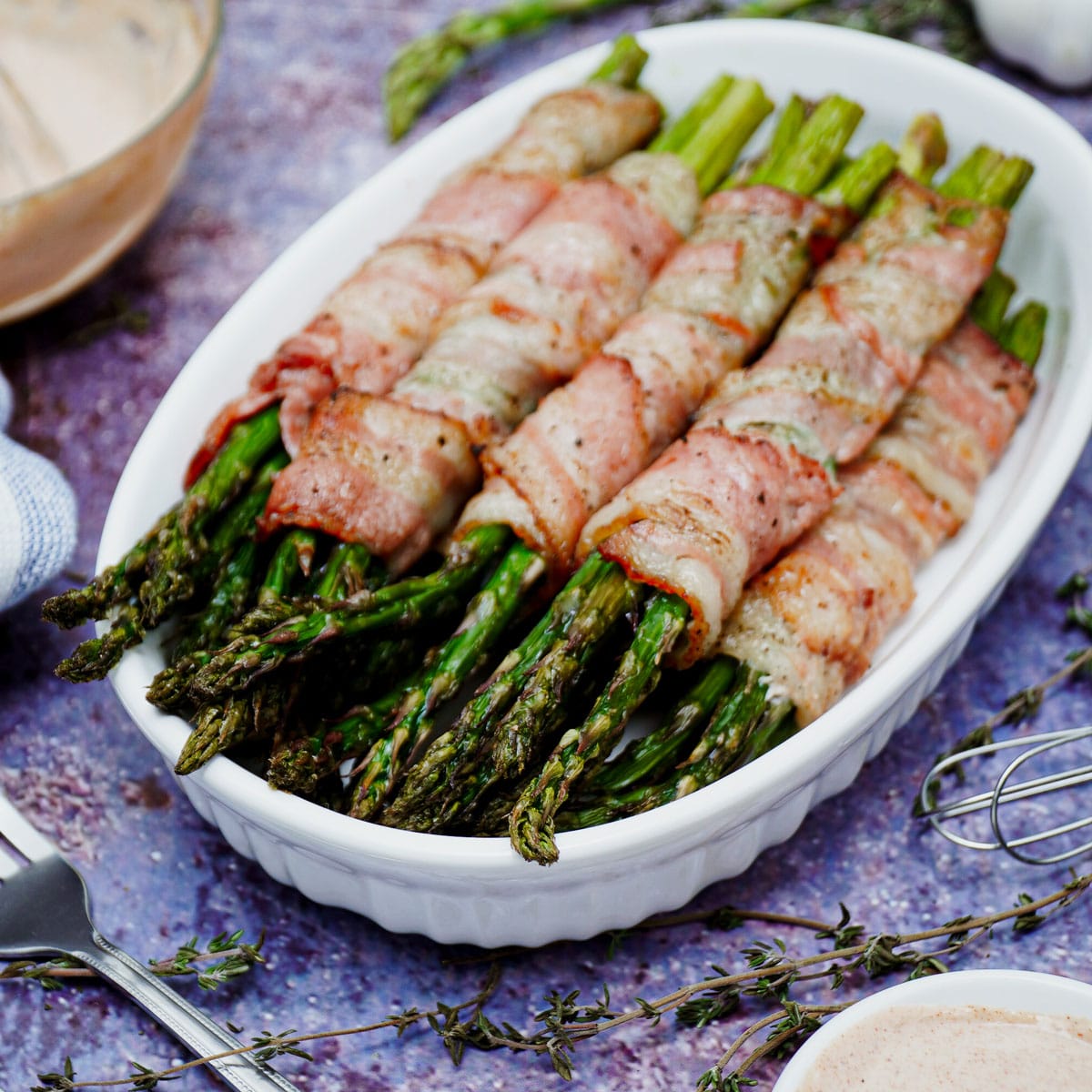 Air fried bacon wrapped asparagus served on a medium-sized baking dish, with yogurt dipping sauce.