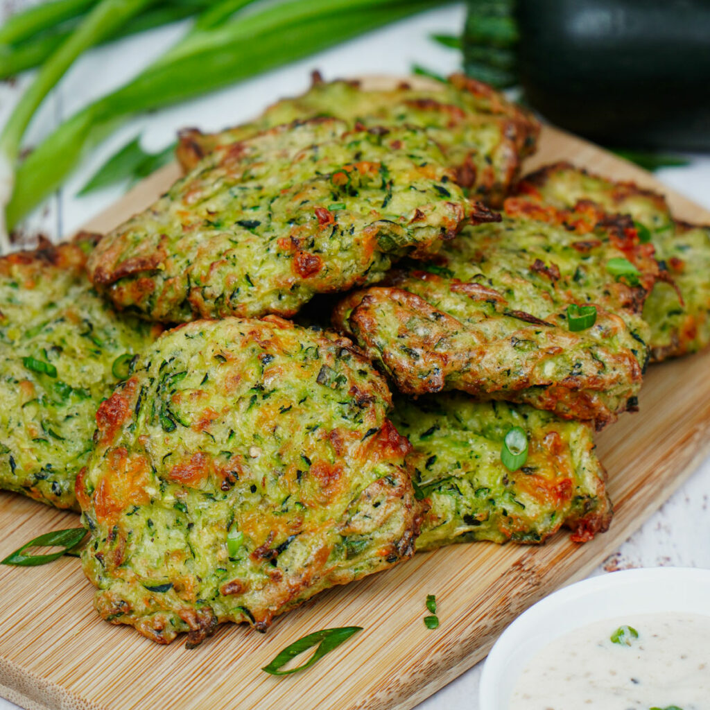 Air fried zucchini fritters served on a bamboo board with ranch dipping sauce.