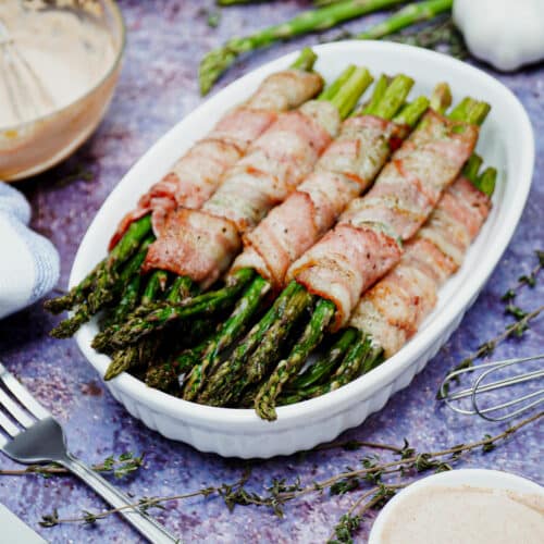 Air fryer bacon wrapped asparagus served on a medium-sized baking dish, with yogurt dipping sauce.
