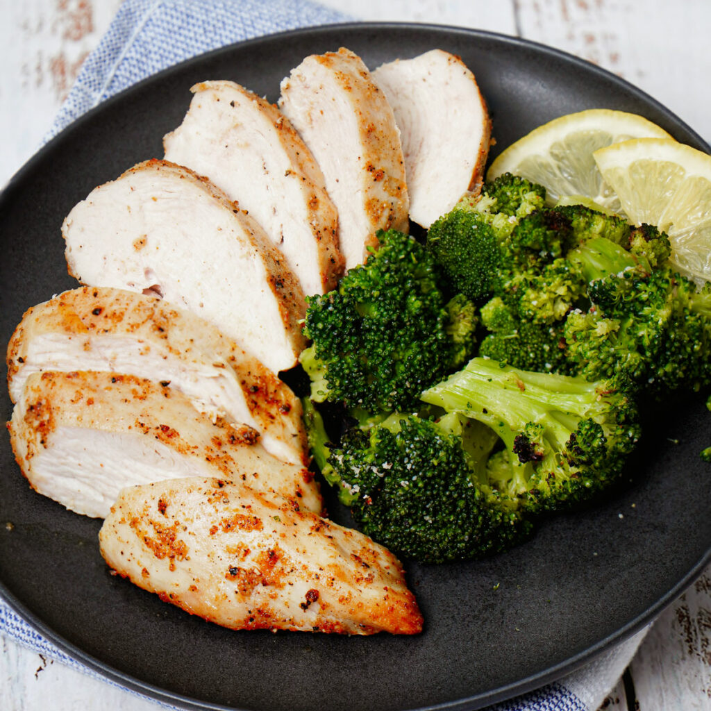 Air fryer frozen chicken breast with air fryer roasted broccoli and lemon slices.
