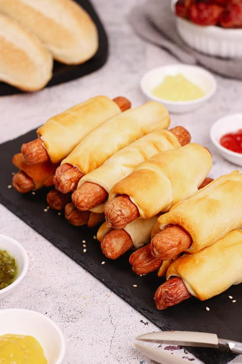 Air fryer pigs in a blanket recipe bite shot, beautifully showcased on a sleek black slate, accompanied by an array of delectable dipping sauces.