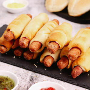 Air fryer pigs in a blanket on a sleek black slate with ketchup, mustard and relish on the side.