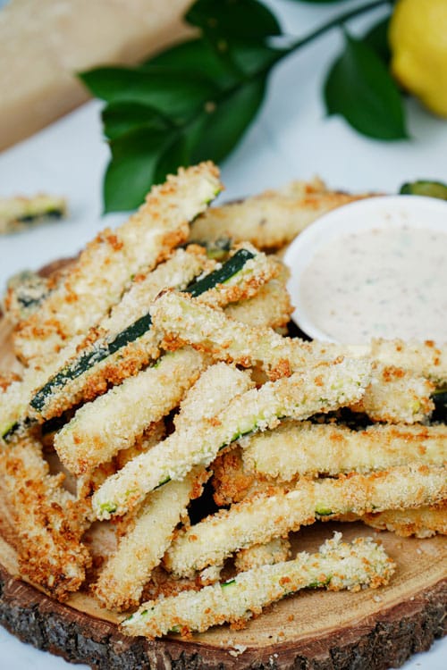Air fryer zucchini fries recipe bite shot, served on a wooden serving board with ranch dipping sauce.