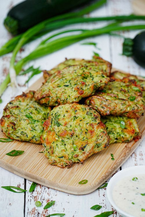 Air fryer zucchini fritters recipe bite shot, served on a bamboo board with ranch dipping sauce.