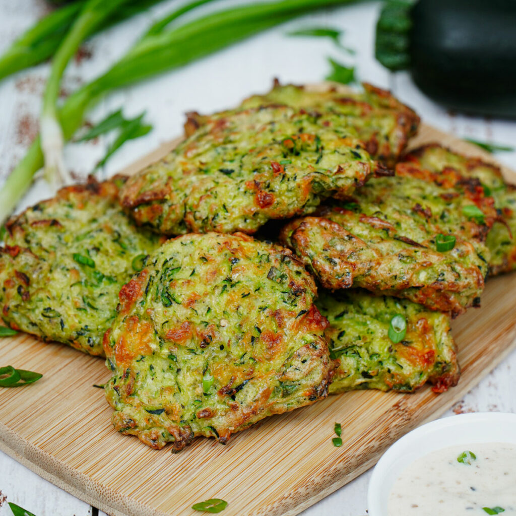 Air fryer zucchini fritters served on a bamboo board with ranch dipping sauce.