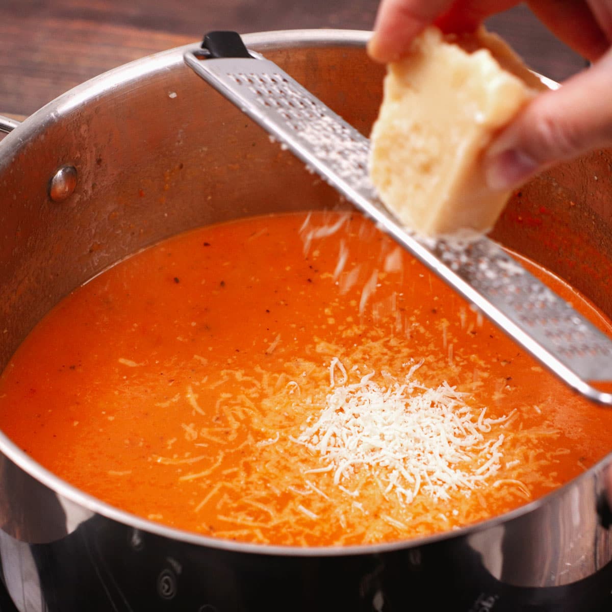 Adding Parmesan cheese to the tomato soup while it's cooking in the pot.