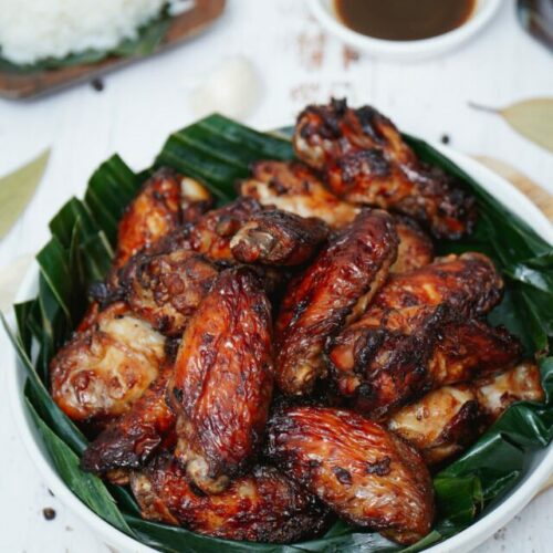 Air fryer adobo chicken wings recipe bite shot, served on a plate with banana leaf.