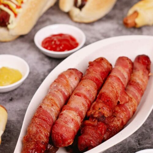 Air fryer bacon wrapped hot dogs recipe bite shot with dipping sauces: relish, mustard, ketchup.