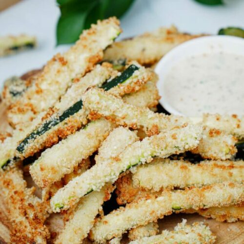 Air fryer zucchini fries recipe bite shot, served on a wooden serving board with ranch dipping sauce.