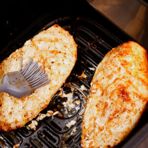 Cooking frozen chicken breast in the air fryer: applying basting sauce.