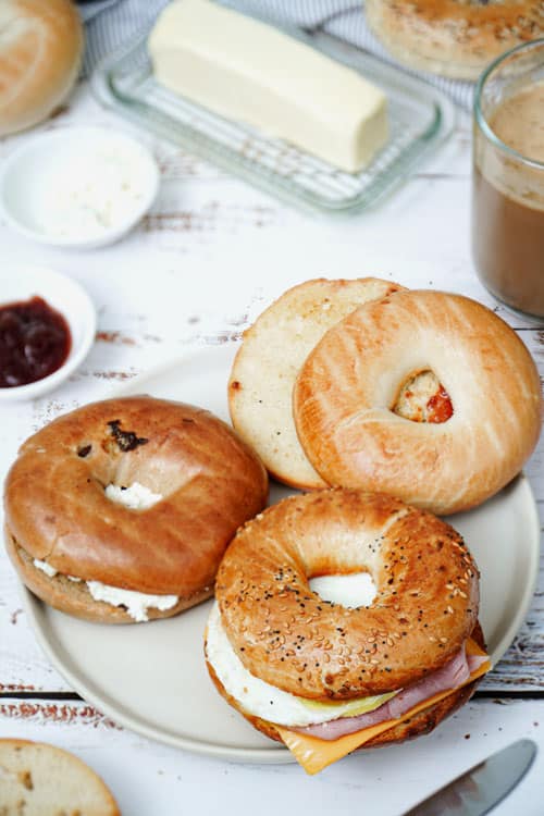 How to Toast Bagel in the Air Fryer recipe bite shot: plain bagel with jam spread, cinnamon raisin bagel with cream cheese, breakfast everything bagel