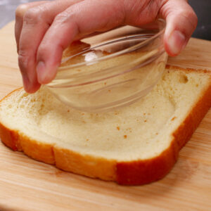 Pressing the bread slice with a small bowl to create a well