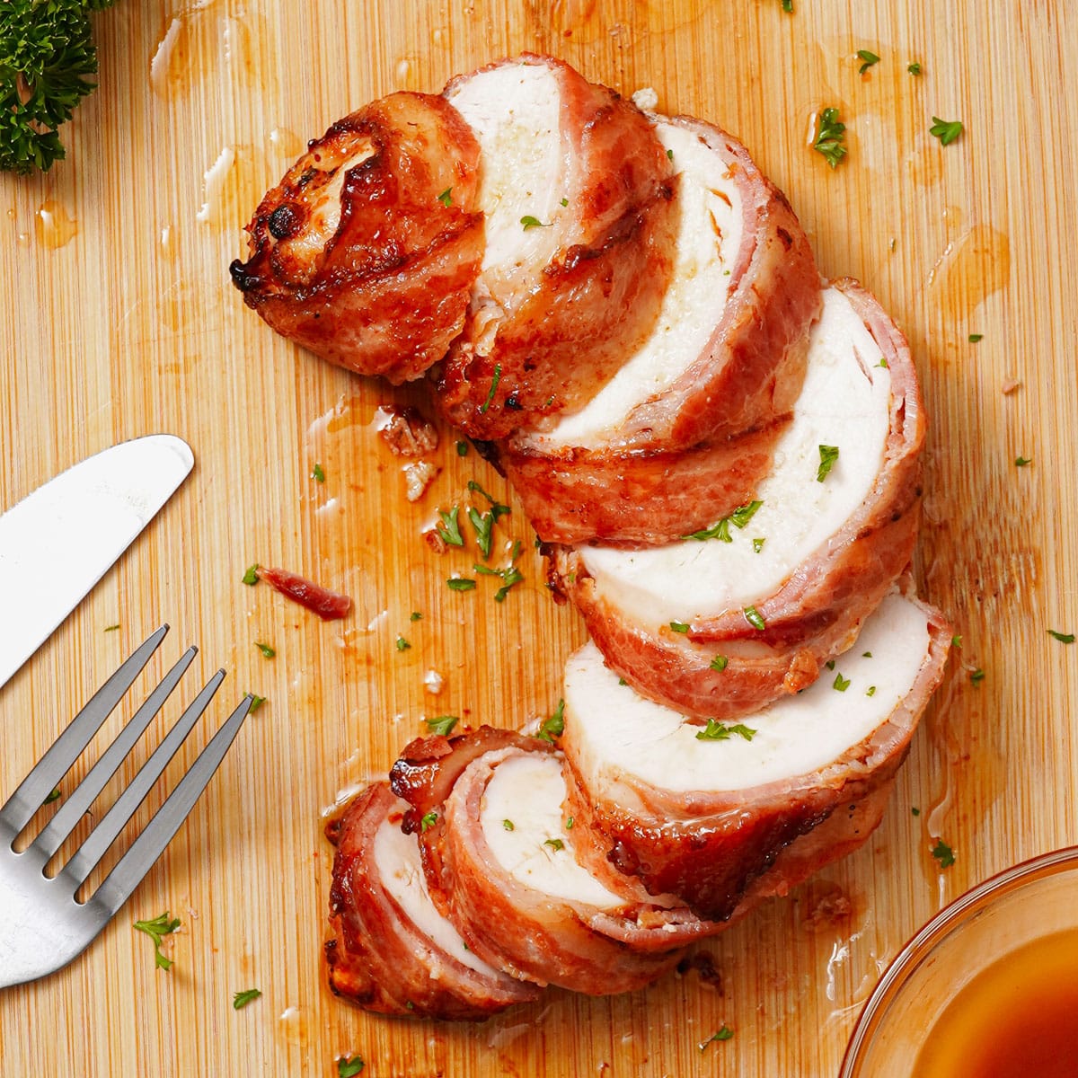 Sliced air fried bacon wrapped chicken breast on a bamboo chopping board.