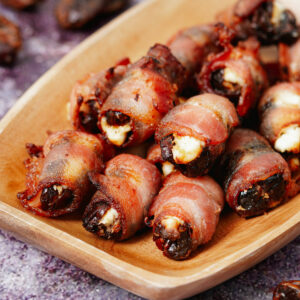 Air fried bacon wrapped dates in a small wooden tray.