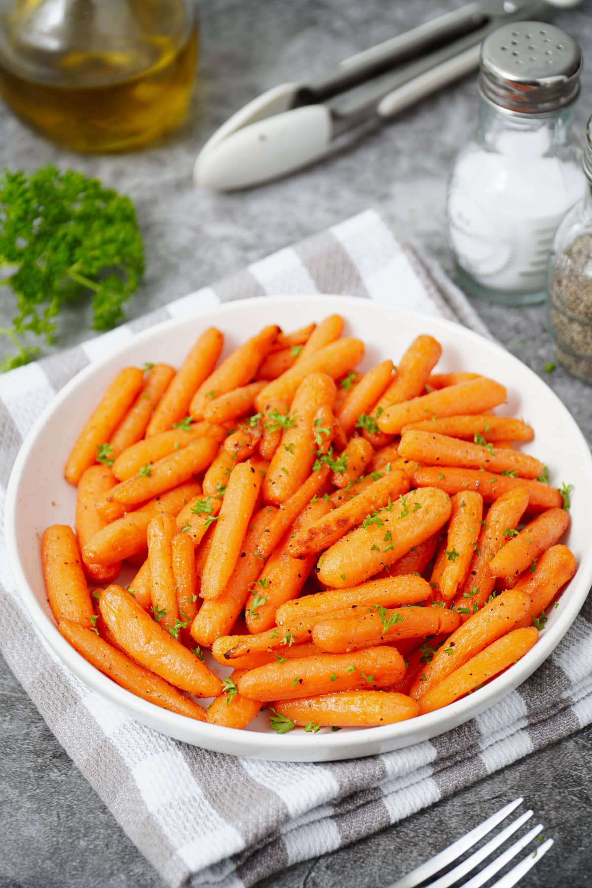 Air fryer baby carrots recipe bite shot, served on a white plate with garnish of fresh parsley.