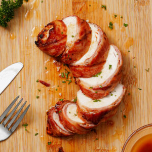 Sliced air fryer bacon wrapped chicken breast on a bamboo chopping board.