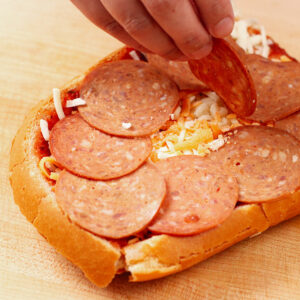 Adding toppings to French bread pizza