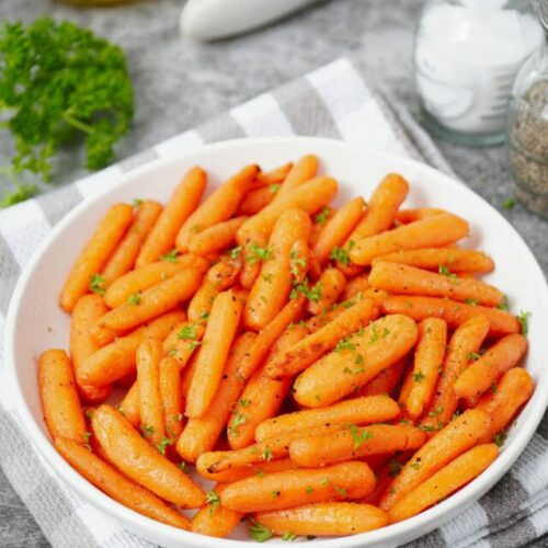 Air fryer baby carrots recipe bite shot, served on a white plate with garnish of fresh parsley.