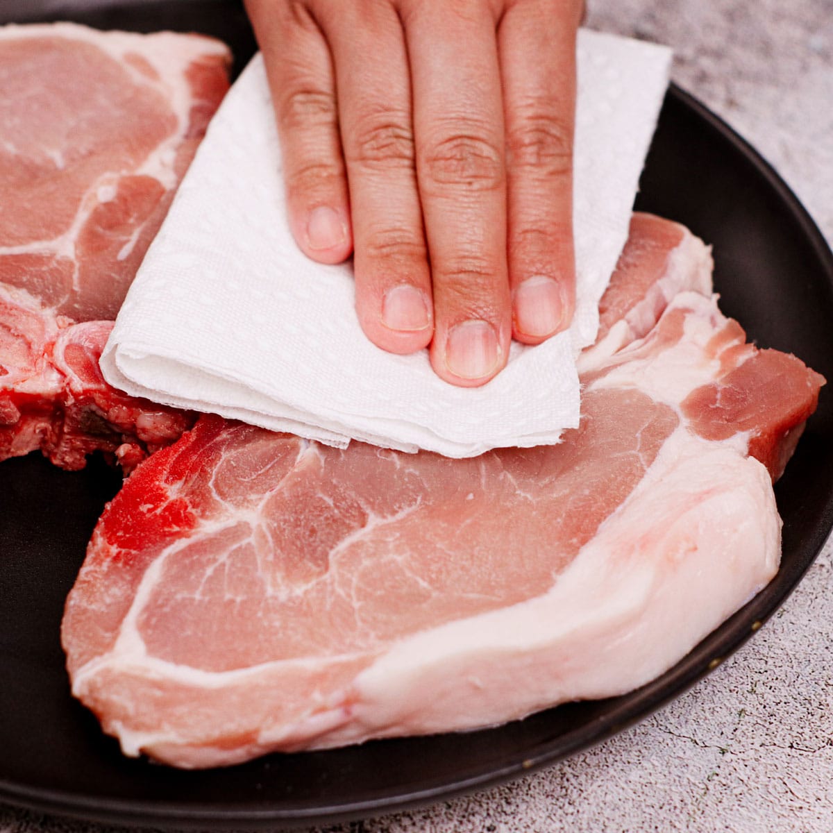 Patting pork chops dry with kitchen towel