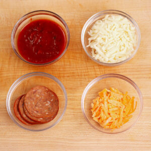 Pizza toppings: pizza sauce, mozzarella cheese, pepperoni slices, cheddar cheese.