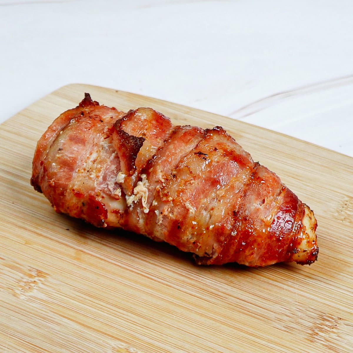 Air-fried bacon-wrapped chicken breast resting on bamboo chopping board.