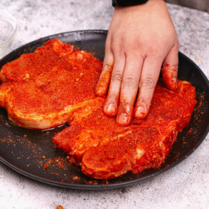 Rubbing seasonings onto raw bone-in pork chops
