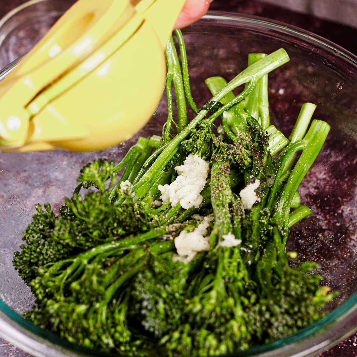 Seasoning broccolini with crushed garlic, olive oil, salt, pepper