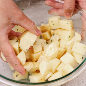 Seasoning cubed potatoes with avocado oil, garlic powder, rosemary, salt and pepper