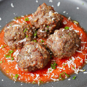 Air fried meatballs, served in a black plate with marinara sauce, sprinkled with grated Parmesan cheese and chopped parsley