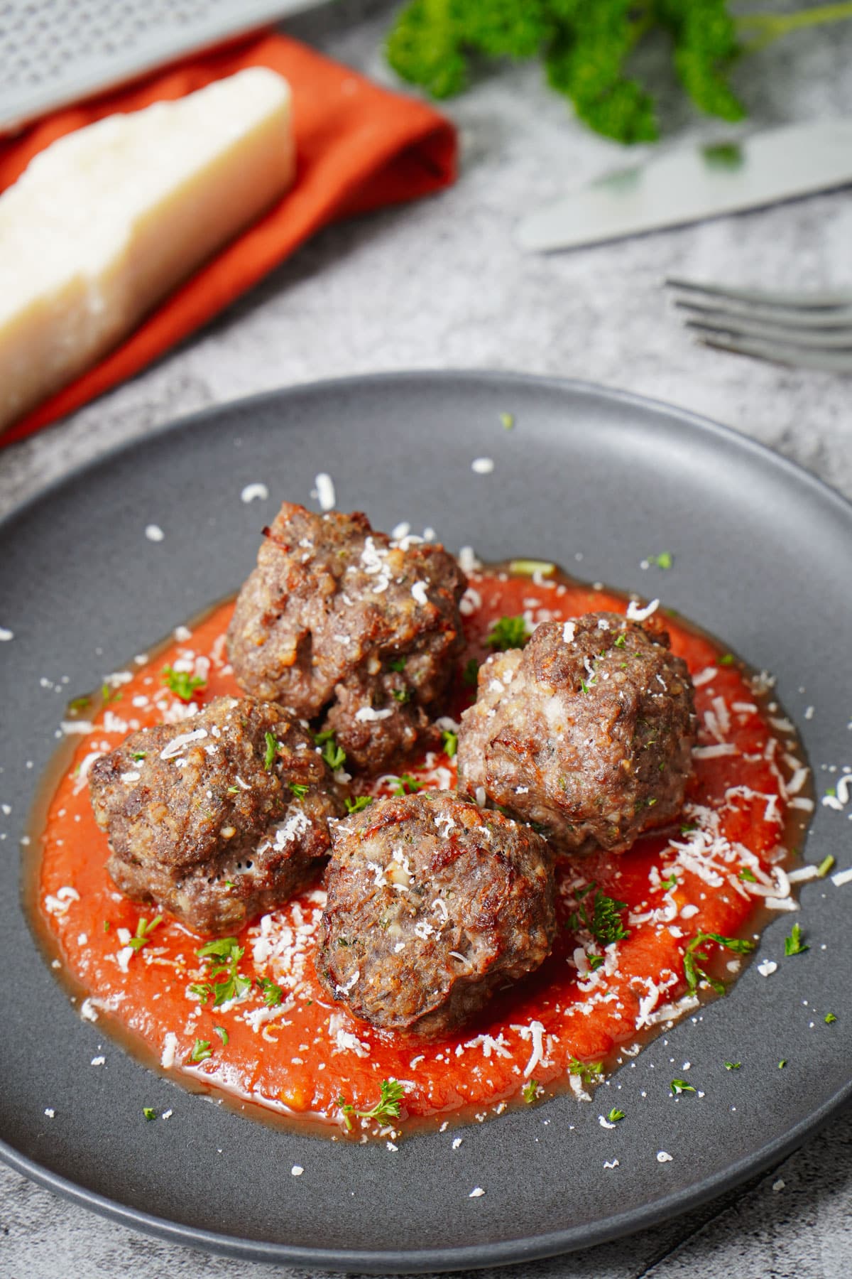 Air fryer meatballs recipe bite shot, served in a black plate with marinara sauce, grated Parmesan cheese and chopped parsley