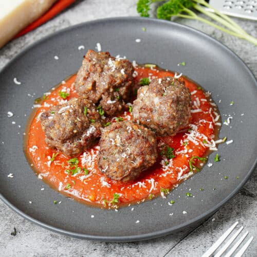 Air fryer meatballs in a black plate with marinara sauce, sprinkled with grated Parmesan cheese and chopped parsley