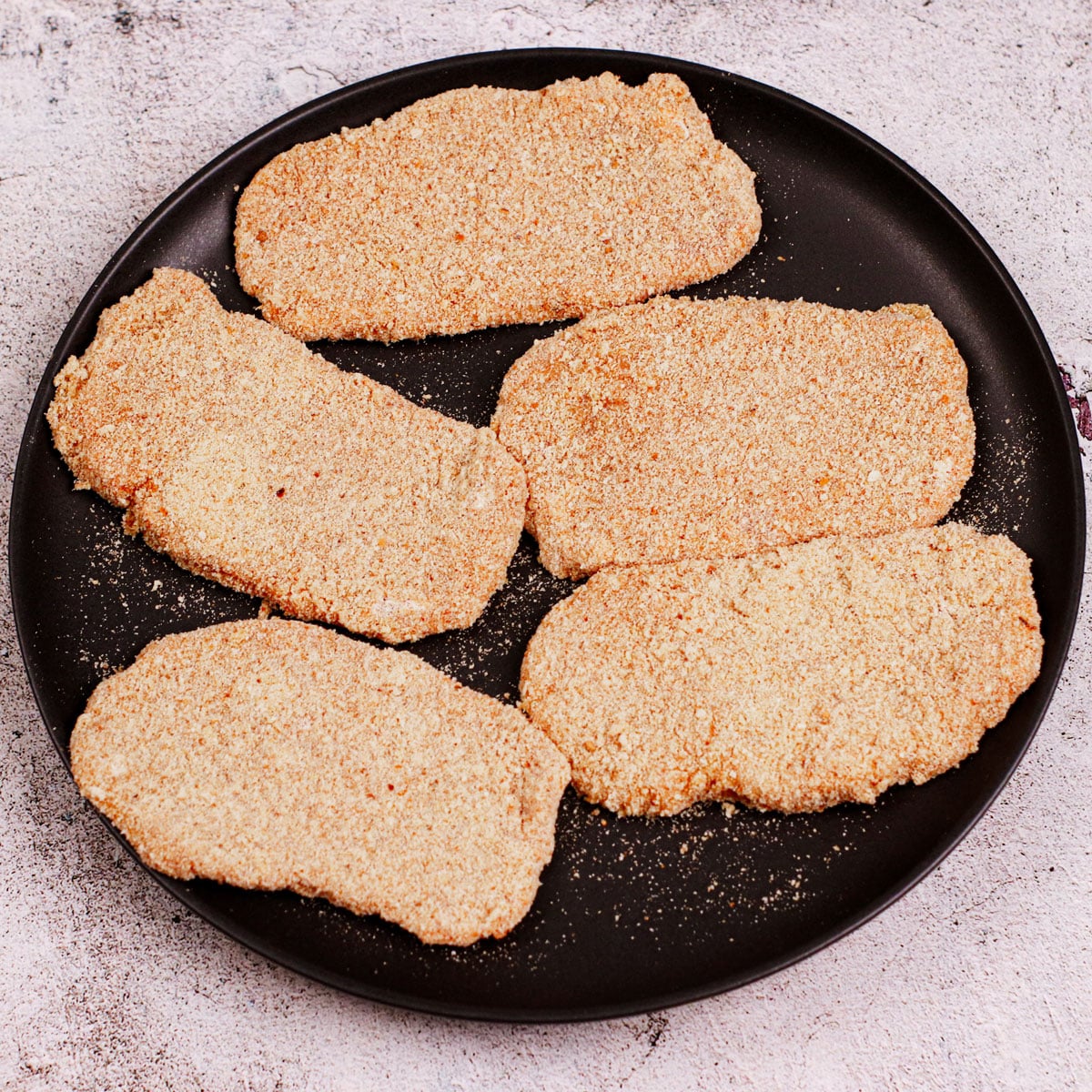 Breaded pork schnitzels on a black plate.