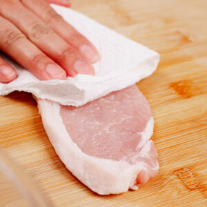 Patting boneless, skinless pork chops dry with kitchen towel.