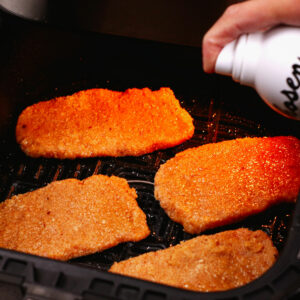 Spraying pork schnitzel with cooking oil