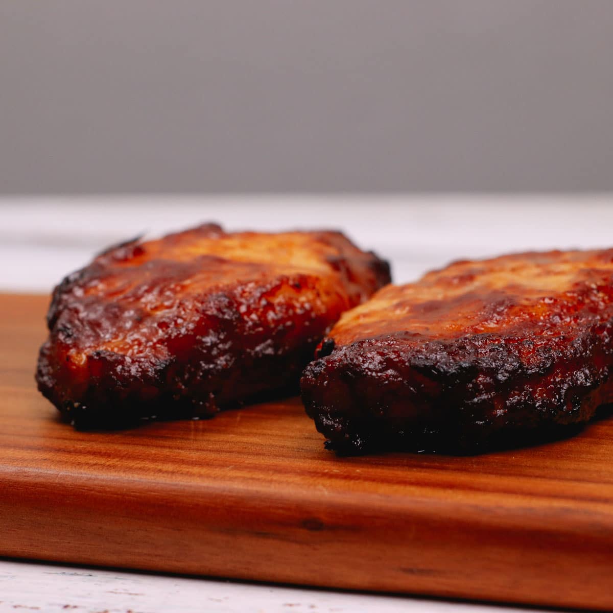 Cooked barbecue flavored pork chops resting on a chopping board.